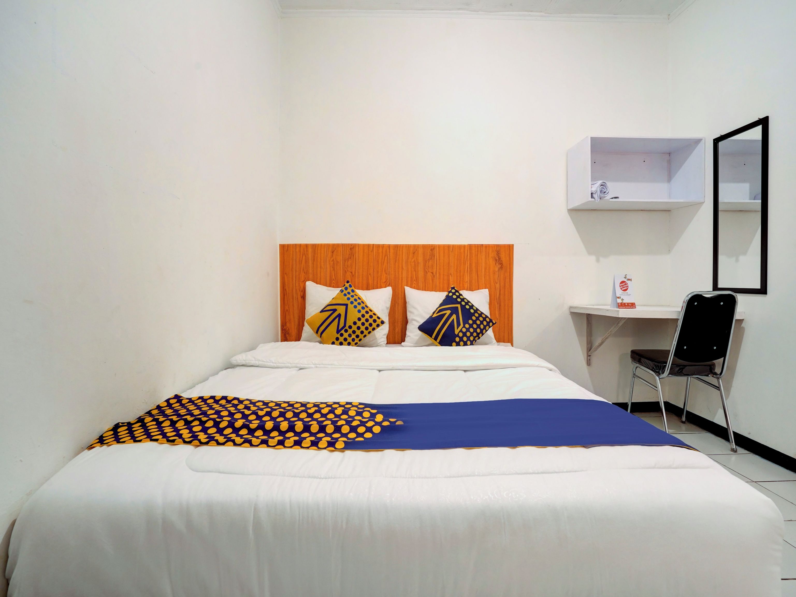 A hotel room with a bed, two pillows, a desk, a chair, and a mirror.