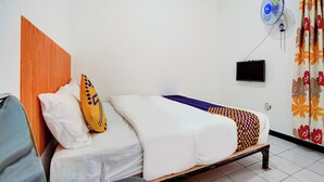 Ett hotellrum med en sänggavel i trä, en säng med vita sängkläder och ett mönstrat överkast, ett litet bord, en väggmonterad TV och en takfläkt.