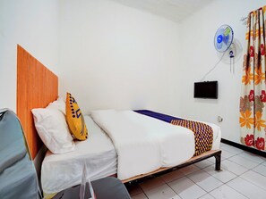A hotel room with a wooden headboard, a bed with white and patterned bedding, a small table, a wall-mounted TV, and a ceiling fan. - Spot ON 90200 Pondok Sabaraya Cileunyi Syariah (Cileunyi)