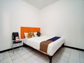 A hotel room with a wooden headboard, a bed with white bedding and patterned pillows, a chair with a coffee maker, and tiled flooring. - Spot ON 90200 Pondok Sabaraya Cileunyi Syariah (Cileunyi)