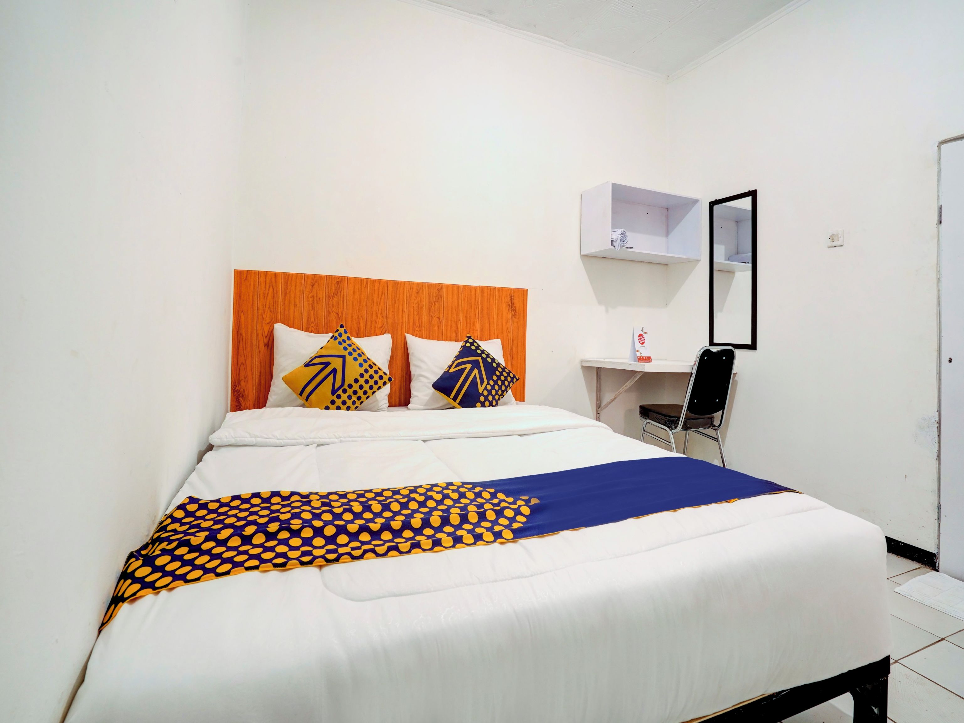 A hotel room with a bed, a wooden headboard, two pillows, a desk with a chair, and a mirror.