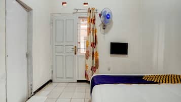 A bedroom with a bed, a door, a wall-mounted TV, and a standing fan.