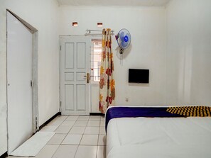 A bedroom with a bed, a door, a wall-mounted TV, and a standing fan. - Spot ON 90200 Pondok Sabaraya Cileunyi Syariah (Cileunyi)