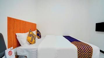 A hotel room with a wooden headboard, a bed with white bedding, two decorative pillows, a blanket with a polka dot pattern, and a flat-screen TV mounted on the wall.