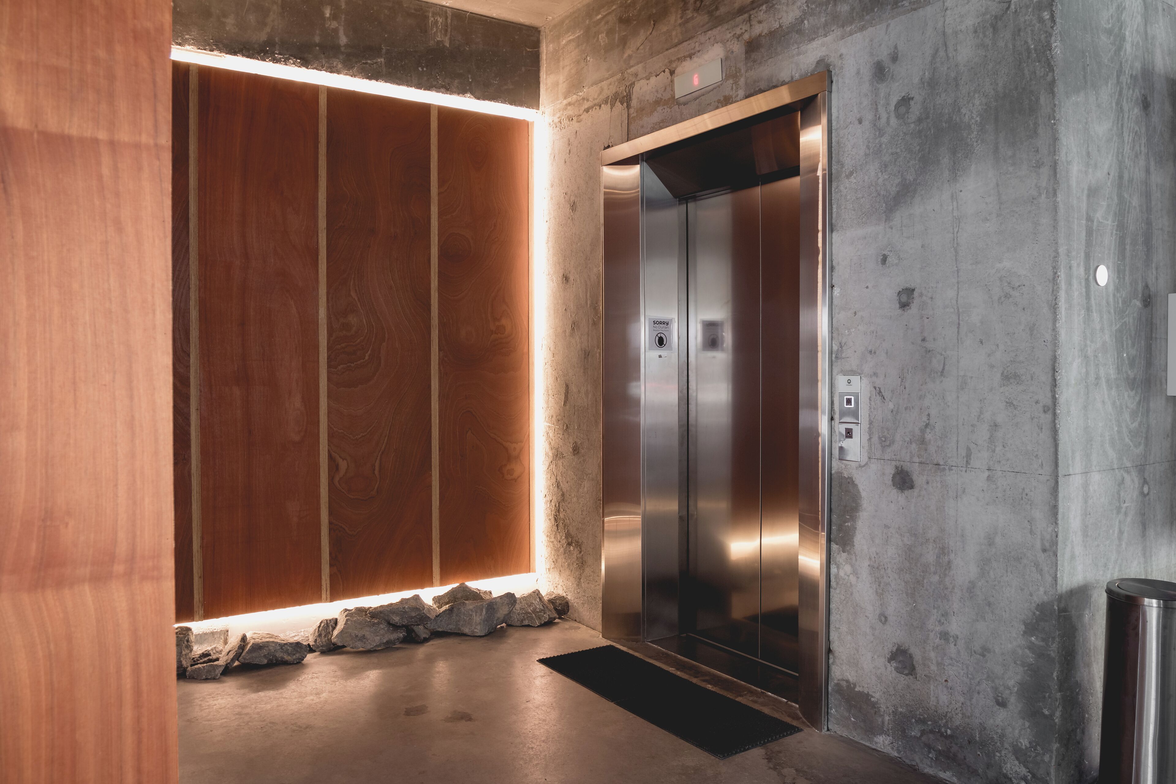 Ein Aufzug mit metallischem Innenraum und Bedienfeld, neben einer Wand mit Holzverkleidung und einer Lichtleiste.