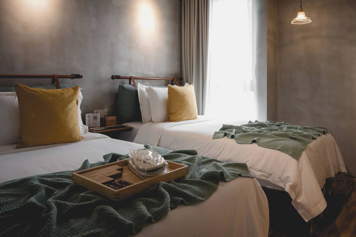 A hotel room with two beds, a tray with a bowl and a book, and a window with curtains.