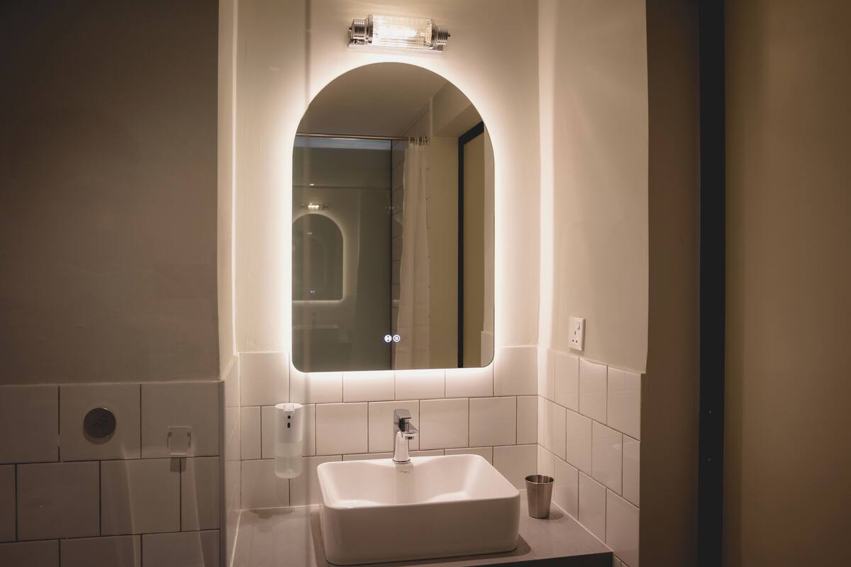 A bathroom with a white sink, a mirror with an arch, and a light fixture above the mirror.