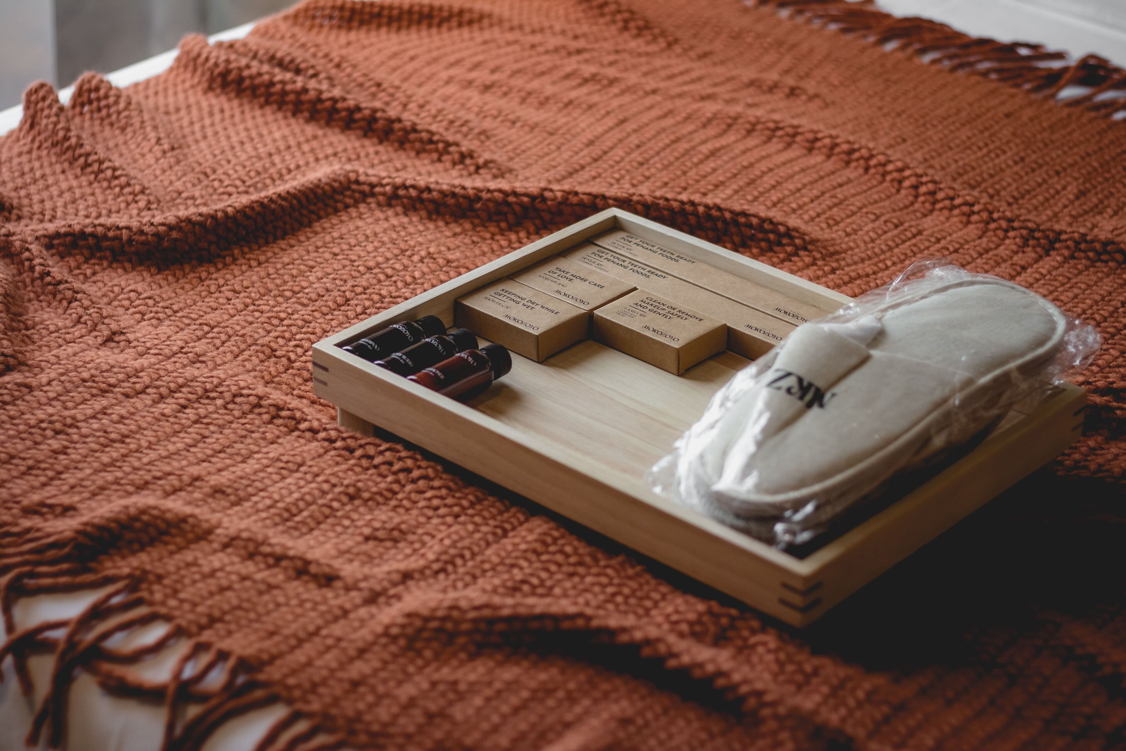 Ein hölzernes Tablett mit Kisten und Flaschen auf einer gemusterten, braunen Decke.