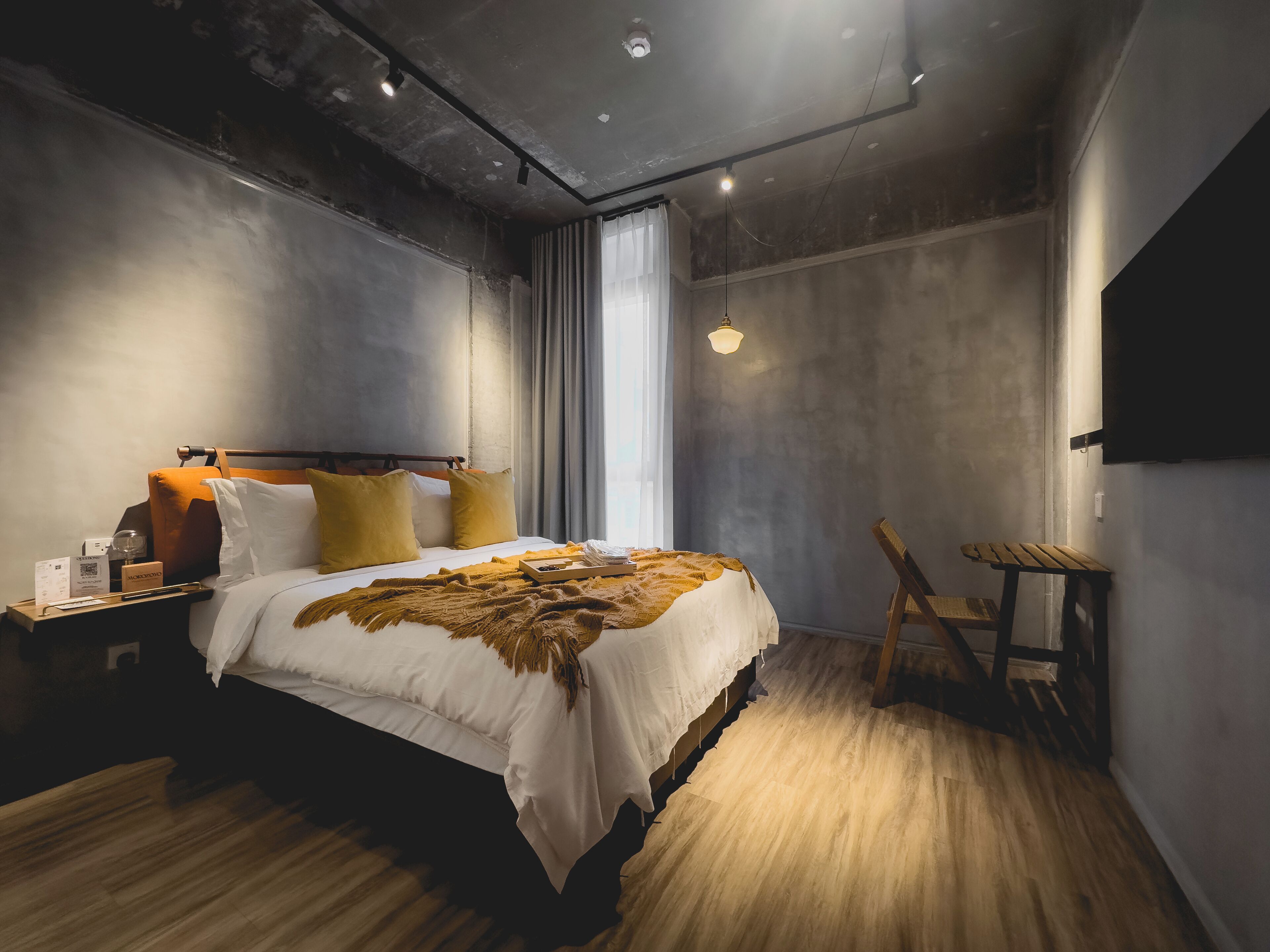 A modern bedroom with a large bed, wooden floor, and a view of the outdoors through a window.