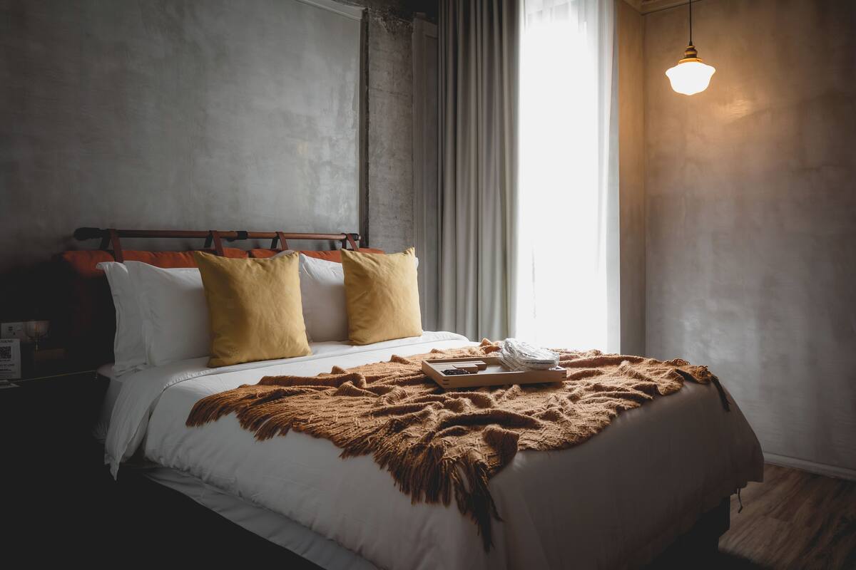 A neatly made bed with a wooden headboard, a brown throw blanket, and a tray with items on it.