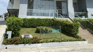 Un immeuble moderne à plusieurs étages, doté de balcons, d’un escalier et d’une enseigne indiquant « OCEAN DRIVE, maison de plage ».
