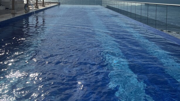 Une piscine à débordement offrant une vue imprenable sur l’océan, un espace salon couvert et une balustrade en verre.