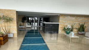 Un hall d’entrée moderne agrémenté d’un élément décoratif aquatique en verre, de murs en pierre et de plantes en pot.