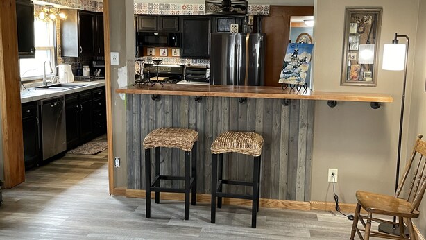 A kitchen with a wooden island, two stools, a refrigerator, and a dining area with a chair. - Limestone Corner Bungalow (Graytown)