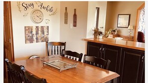 A dining area with a wooden table, black chairs, and a glass tray. There are wall decorations including a clock and framed pictures. - Limestone Corner Bungalow (Graytown)