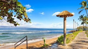 A beach with a stone pathway, a caution sign, and a thatched umbrella.
