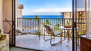 A balcony with two lounge chairs, a small table, and a view of the ocean.