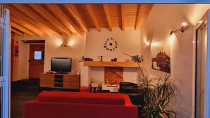 Un salon chaleureux avec un canapé rouge, un téléviseur, une cheminée et une horloge au mur.