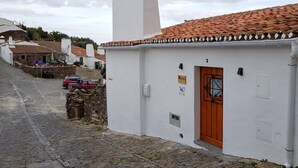 Un bâtiment blanc, avec un toit en tuiles et une porte en bois, situé dans une rue pavée.