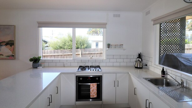 A compact kitchen with white cabinetry, a built-in oven, a gas stove, a sink, and a window with a view of the outside. - 9 Bastion Point Road (Mallacoota)