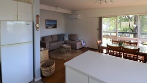 A compact living space with a kitchenette, a dining area, and a seating area with a view of the outdoors. - 9 Bastion Point Road (Mallacoota)