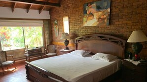 Een ruime slaapkamer met een groot bed, een houten hoofdeinde, een bakstenen muur en een schilderij.