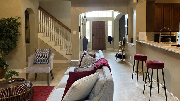 Un vaste espace de vie doté d’un haut plafond, d’un escalier, d’une cuisine équipée d’appareils modernes et d’un coin salon avec un canapé et des fauteuils.