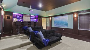Une salle de cinéma privée dotée d’un grand écran, de plusieurs espaces de détente et d’un bar avec un éclairage d’ambiance.
