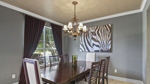 Une salle à manger avec une grande table, des chaises, un lustre et une décoration murale à motifs zébrés.