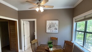 A dining area with a wooden table and chairs, a ceiling fan, and a window with a view of trees. - Peaceful Cabin Overlooking the Bogue Chitto River (franklinton)