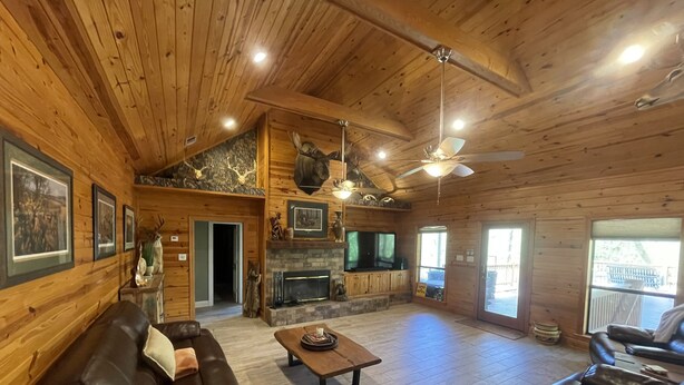 A spacious living room with a fireplace, wooden walls, and a ceiling fan. - Peaceful Cabin Overlooking the Bogue Chitto River (franklinton)
