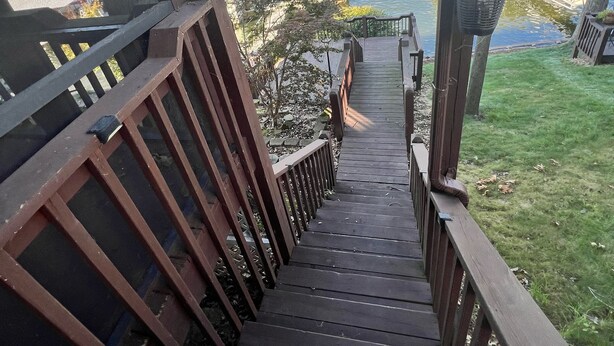 A wooden staircase leading down to a dock by a lake, with a view of houses and boats in the background. - Lake front with orovate dock located in same cove as Coconuts!!! (Gravois Mills)