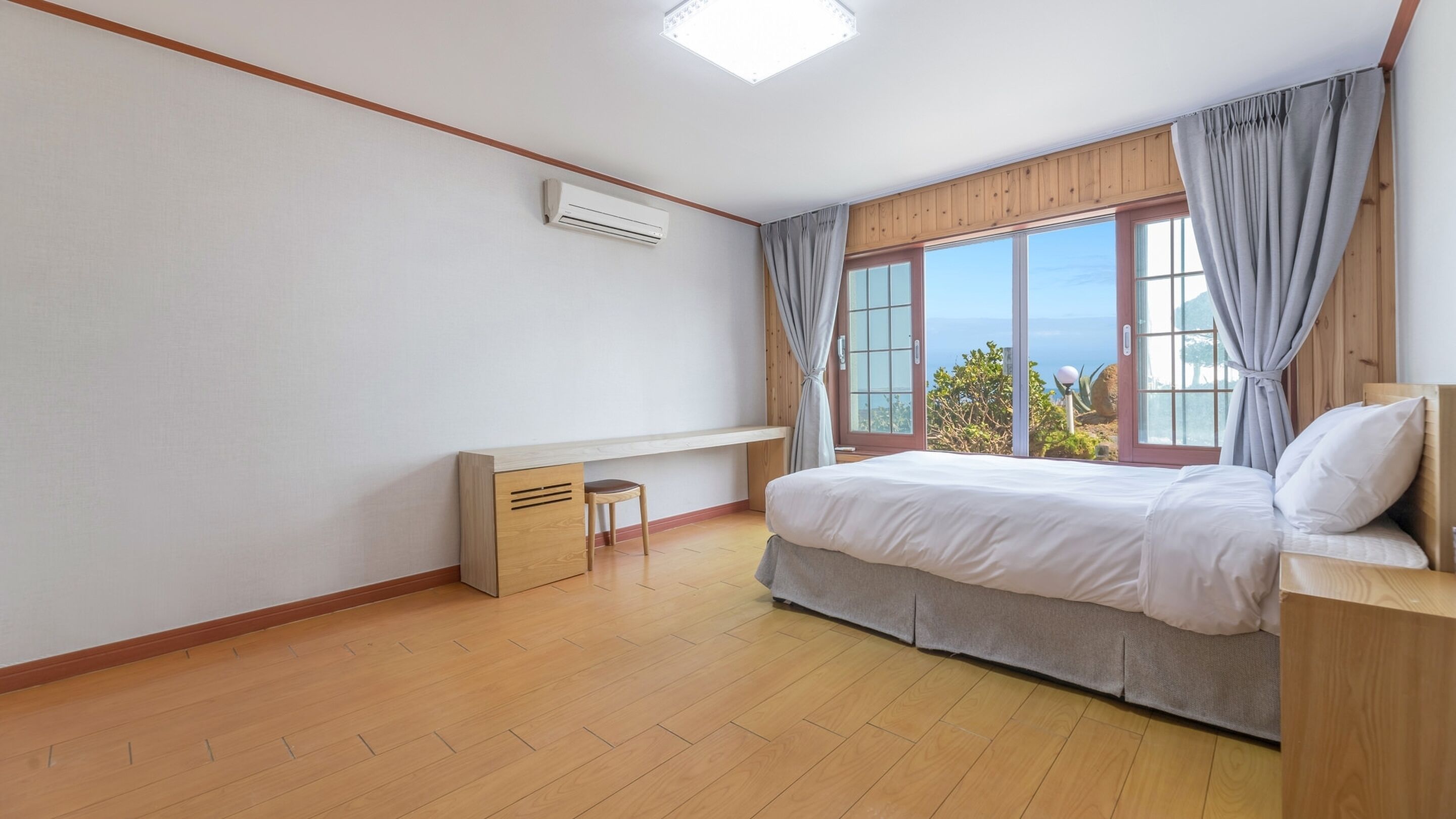 A bedroom with a bed, a desk, and a window with curtains.