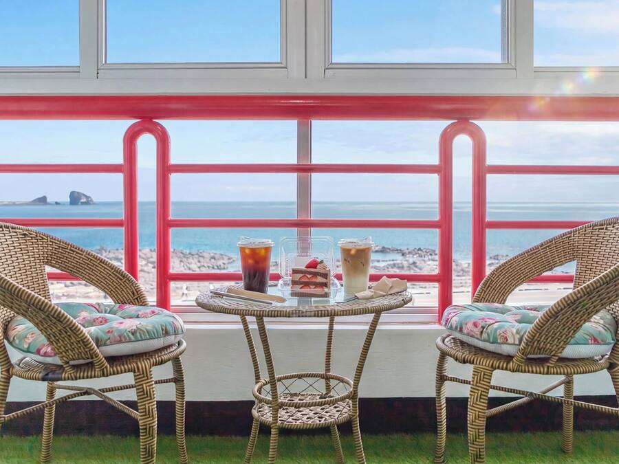 A balcony with wicker chairs, a small table, and a view of the beach and ocean.