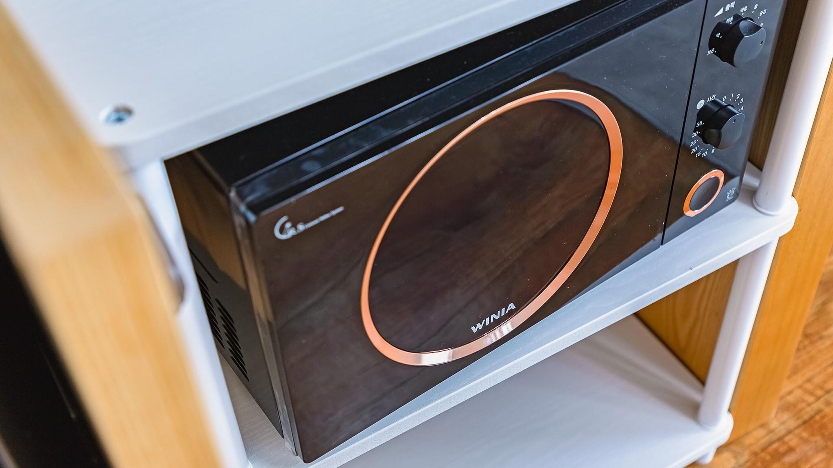 Un horno microondas compacto con pantalla digital y perillas de control, integrado en un gabinete blanco.
