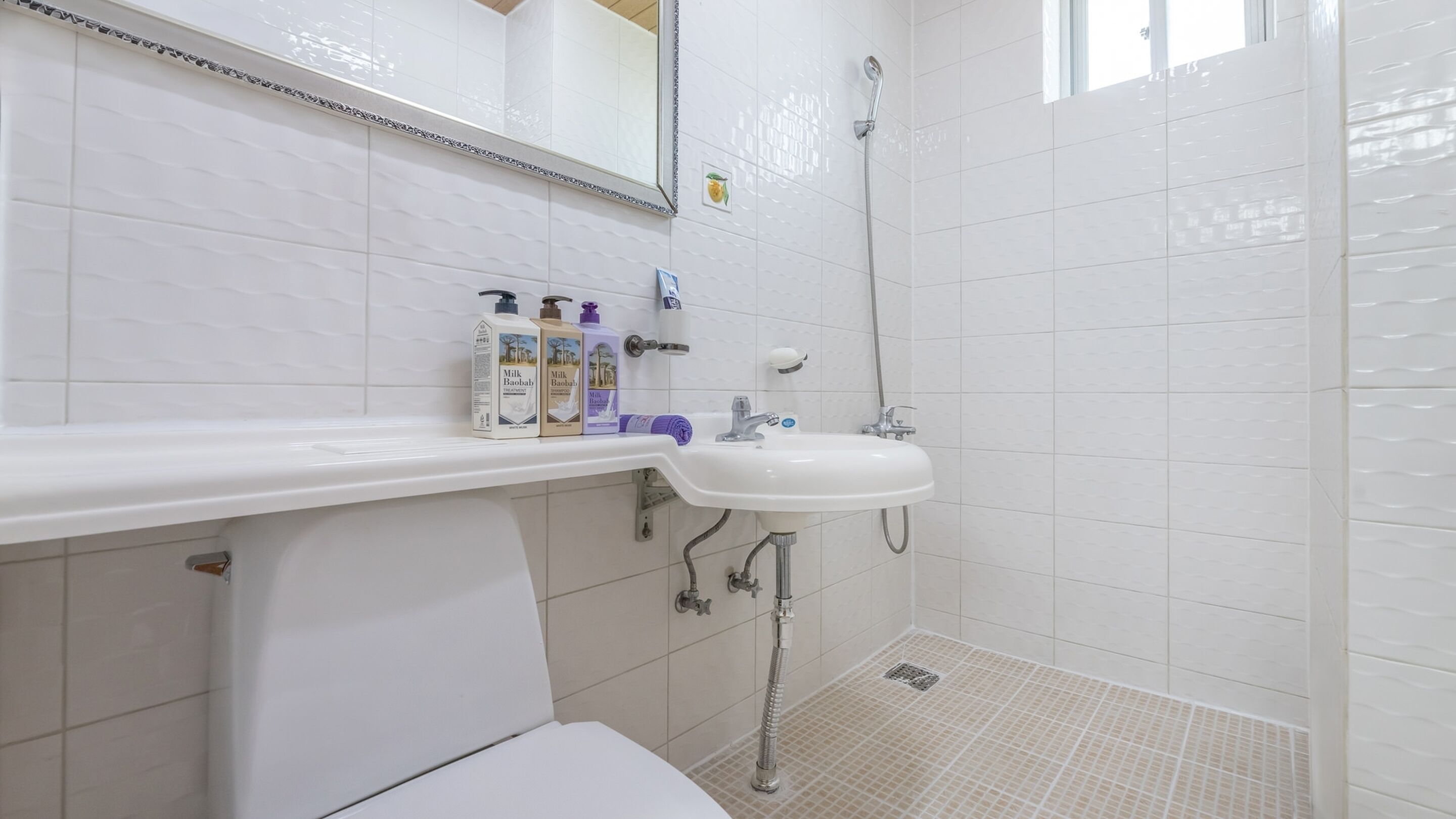 A bathroom with a white sink, mirror, and shower. There are toiletries on the sink counter.