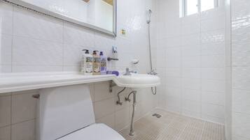 A bathroom with a white sink, mirror, and shower. There are toiletries on the sink counter.