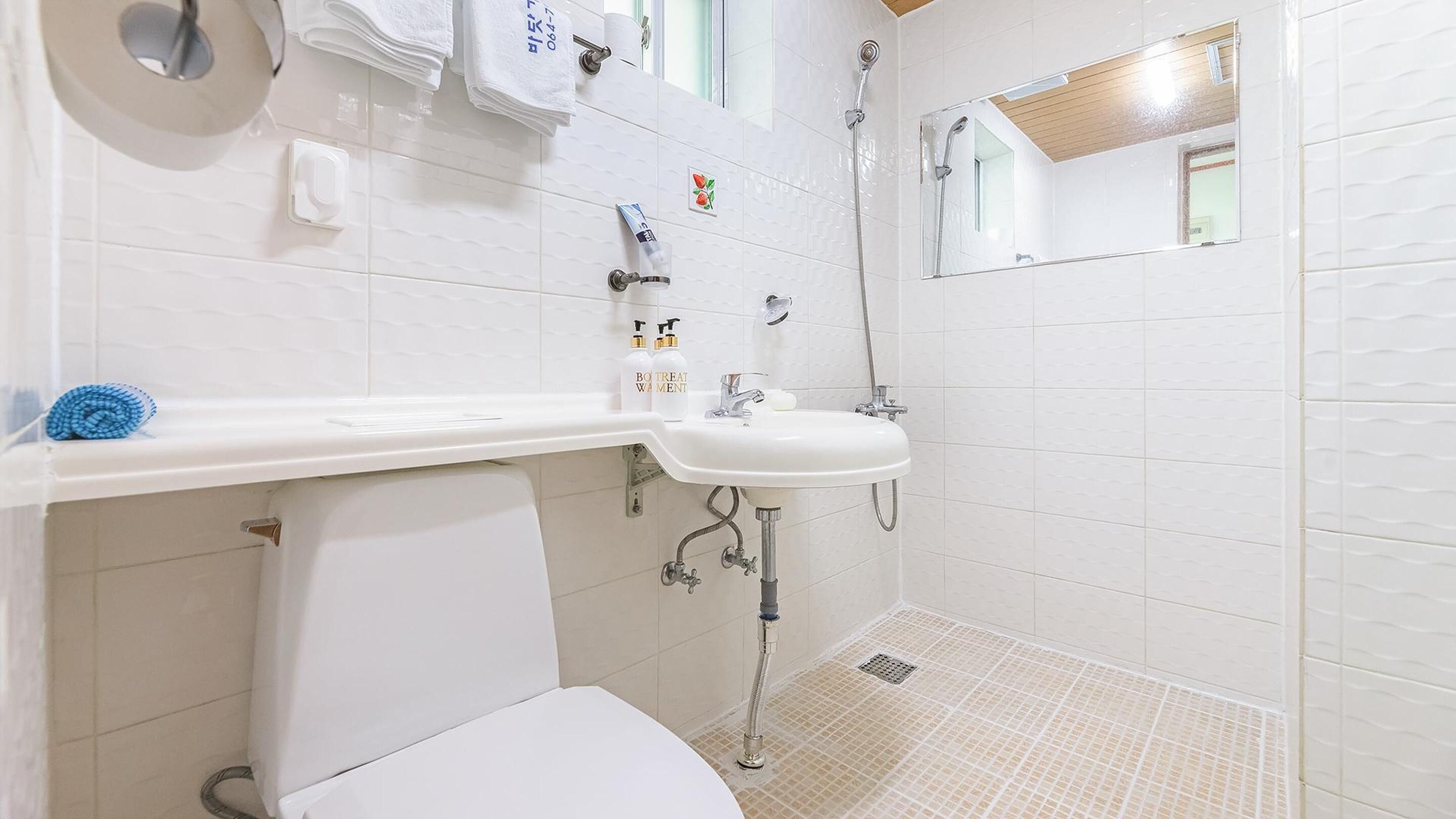 A bathroom with a white sink, a toilet, and a shower. There are towels and toiletries on the wall.