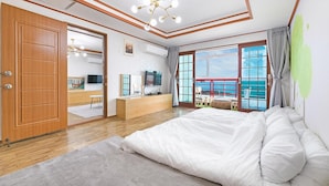 Un dormitorio con una cama grande, un armario de madera, un televisor y un balcón con vistas al mar.