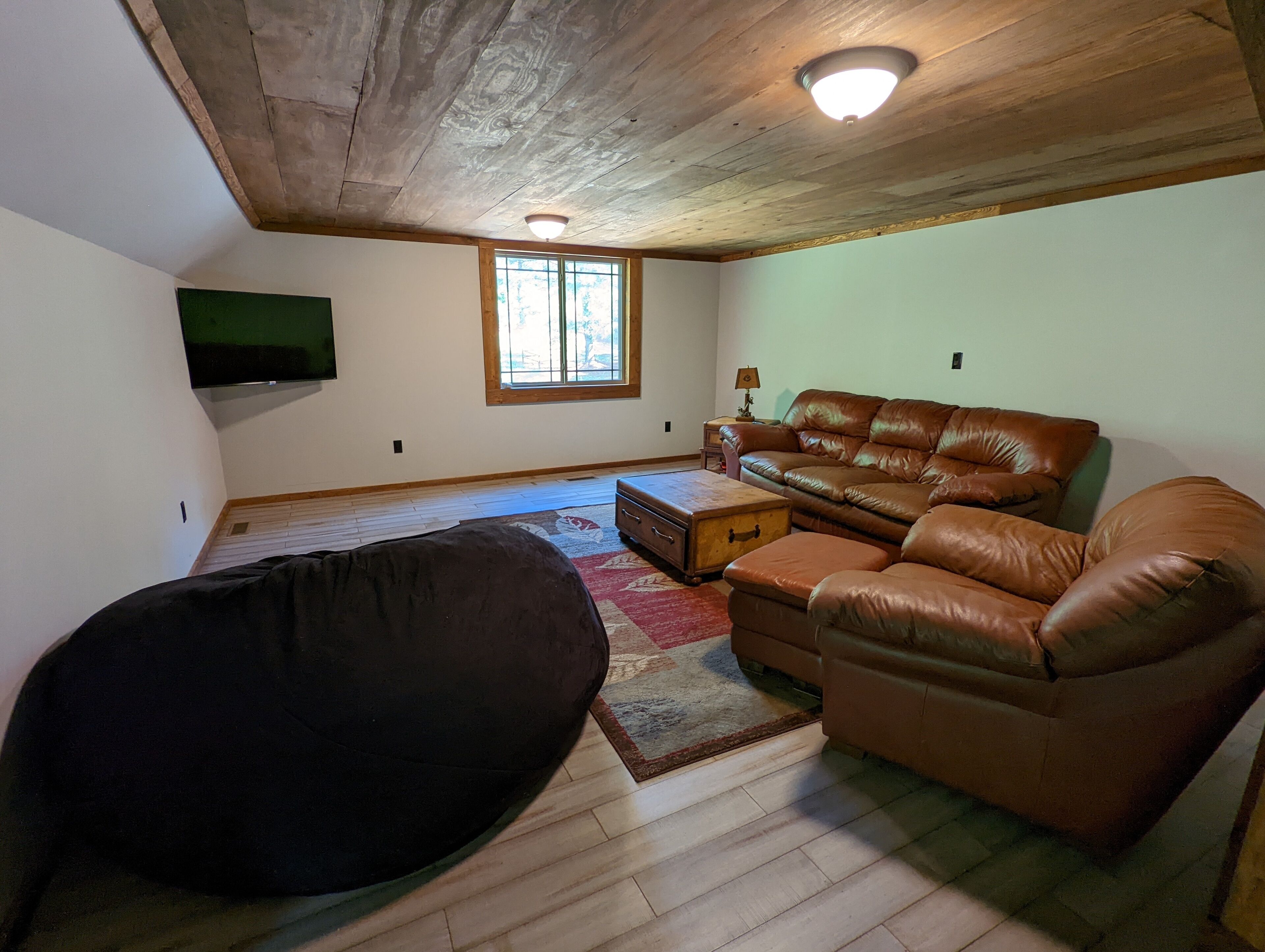 A living room with a brown leather sofa, a black bean bag chair, a wooden coffee table, and a television mounted on the wall.