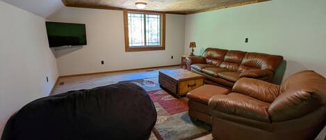 A living room with a brown leather sofa, a black bean bag chair, a wooden coffee table, and a television mounted on the wall.