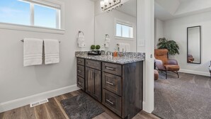 Une salle de bain moderne avec un meuble-lavabo en bois foncé, des serviettes blanches, un grand miroir et une plante en pot.