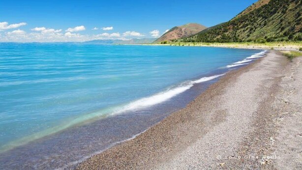 Une plage à l’eau d’un bleu limpide et au rivage de galets.