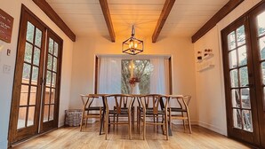 A dining area with a wooden table and chairs, a chandelier, and large windows with curtains. - Secluded 1 acre Mountain Home - Hot Tub, 3 Decks & Direct National Forest Access (Idyllwild-Pine Cove)