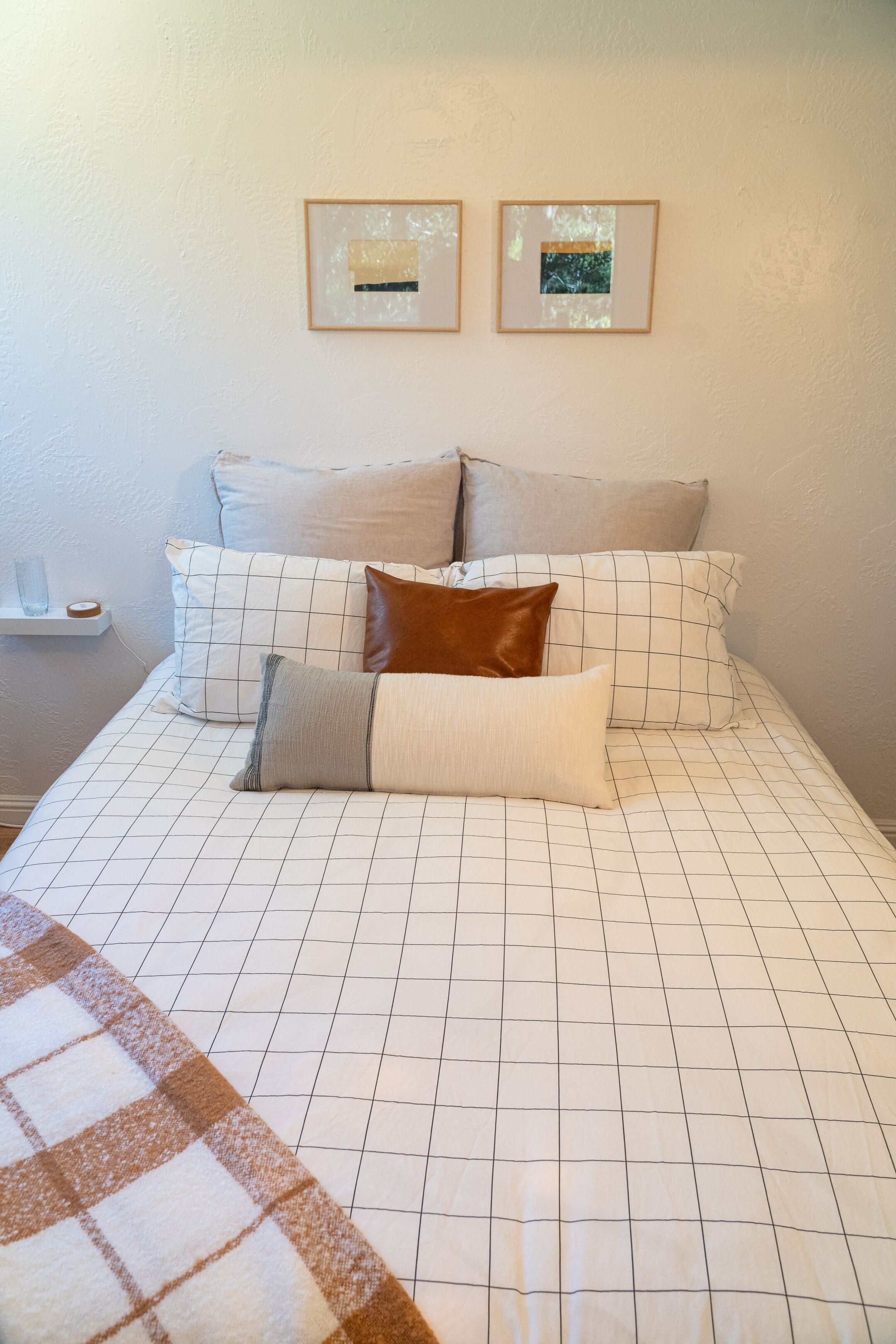 A neatly made bed with a checkered bedspread and multiple pillows. There are two framed pictures on the wall above the bed.