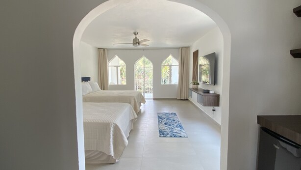 Quarto com duas camas, um ventilador de teto, uma TV e vista para o exterior através de janelas em arco.