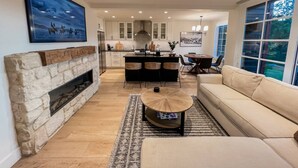 Un salon moderne avec une cheminée en pierre, un canapé beige et un coin repas comprenant une table ronde et des chaises.