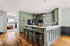 Cozinha moderna com ilha central, banquetas e vista para uma sala de estar.