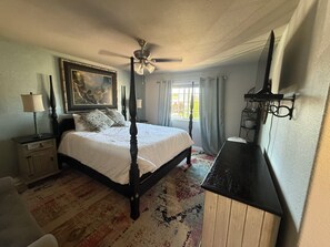 Ein Schlafzimmer mit einem Himmelbett, einem Deckenventilator, einem Gemälde an der Wand und einem Schreibtisch mit einer Lampe.