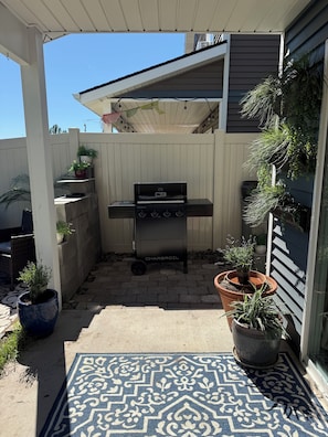 Ein überdachter Patio-Bereich mit Grill, Kübelpflanzen und einem gemusterten Teppich.